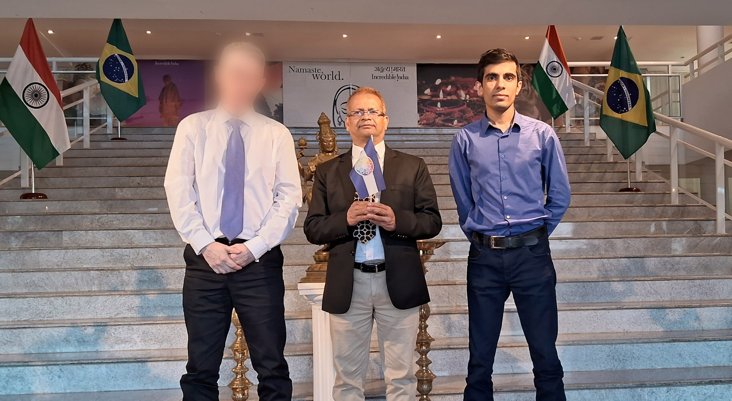 His Excellency the Deputy Ambassador of India in Brasilia, holding the Flag of Autistan in the Embassy of India. (On the left, the founder of the Autistan Diplomatic Organization (who does not wish to be publicly exposed), and on the right, his assistant.)